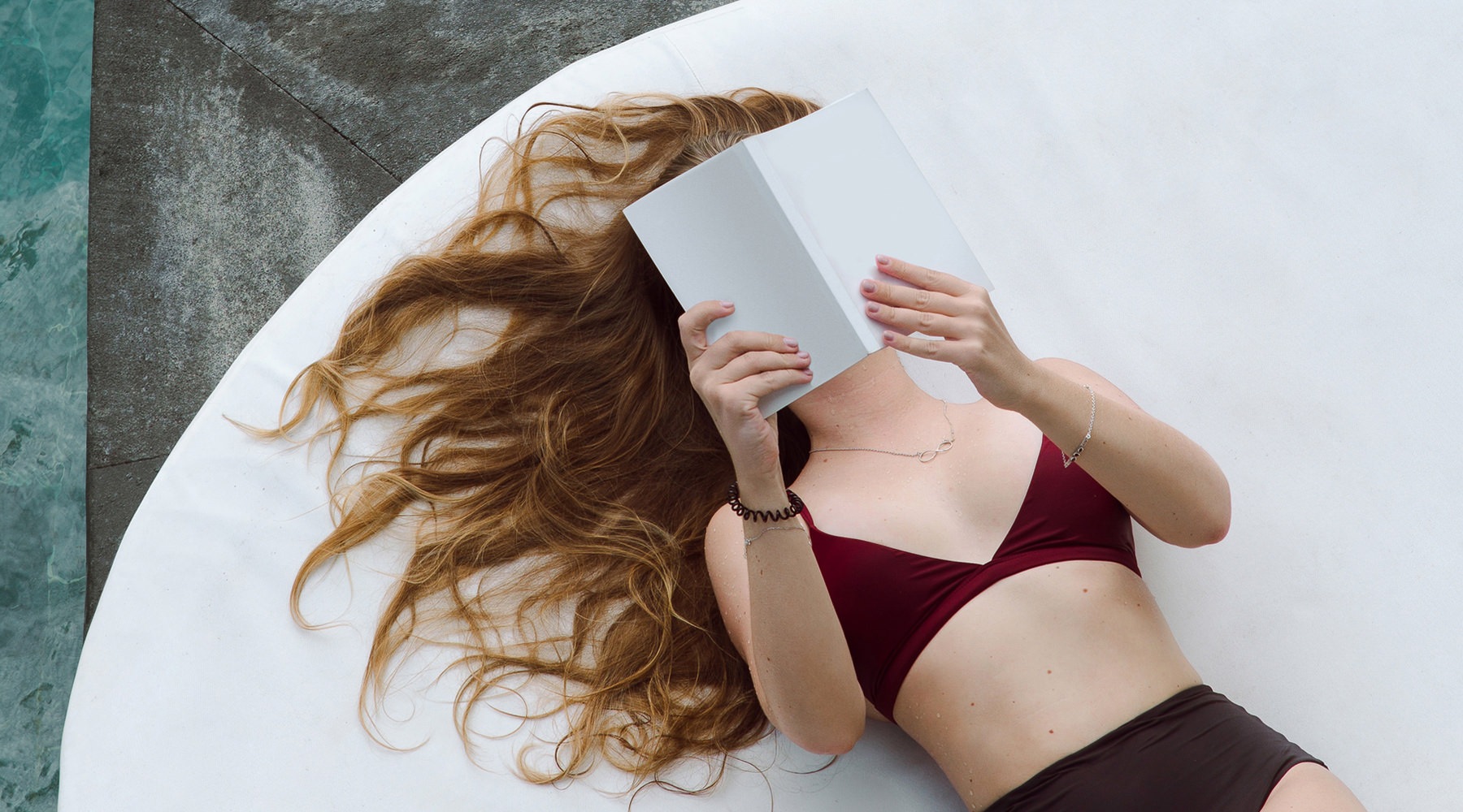 Woman reading a book by the pool 