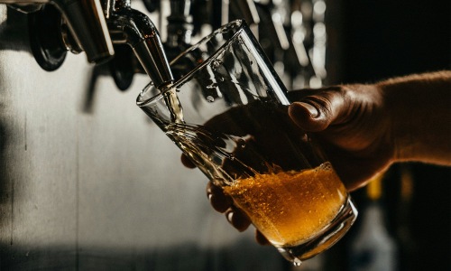 a person pouring a beer off a tap