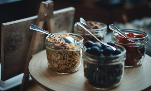 granola and fruit filled jars with spoons on a table